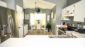 A modern kitchen with stainless steel appliances, a dining area with a table and chairs, and a view of the outdoors through the window.