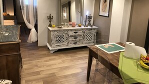 A room with a wooden floor, a white vanity with a mirror, a green table with a fruit bowl, and a framed picture on the wall. - San secondo street (Torino)