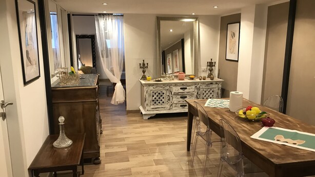A dining area with a wooden table, clear chairs, a white cabinet with drawers, and a mirror above the cabinet. - San secondo street (Torino)