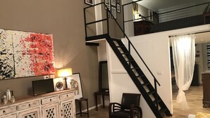 A spacious living room with a high ceiling, a staircase leading to an upper level, a large abstract painting, a wooden coffee table, and a white sofa with a yellow pillow. - San secondo street (Torino)