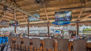 Angolo bar con arredi in legno, diverse schermi e vista sull'acqua.