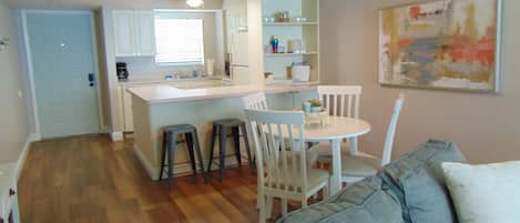 A compact living space with a kitchenette, a dining area with a white table and chairs, and a gray sofa with cushions.