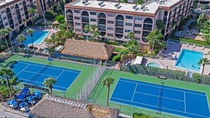 Un hotel con diversi campi da tennis, una piscina e una struttura con tetto di paglia.