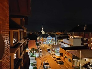 Une vue nocturne d’une rue de la ville, avec des immeubles, une église et des voitures garées.