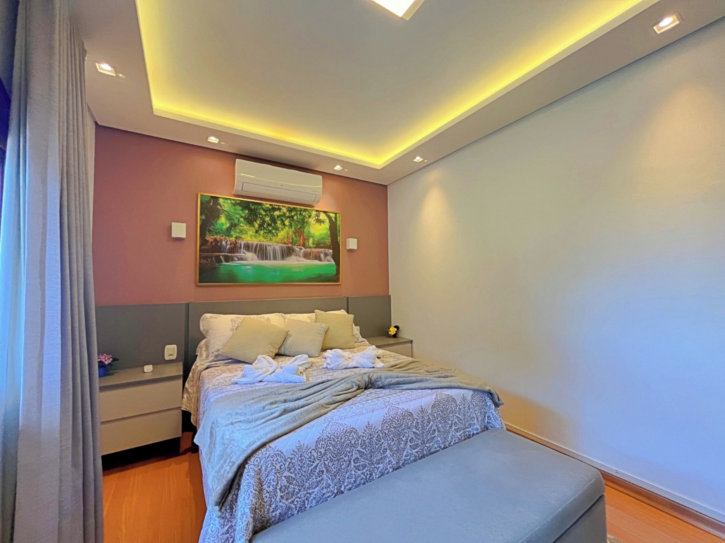 A modern bedroom with a bed, bedside tables, a nightstand, and a wall-mounted air conditioner.