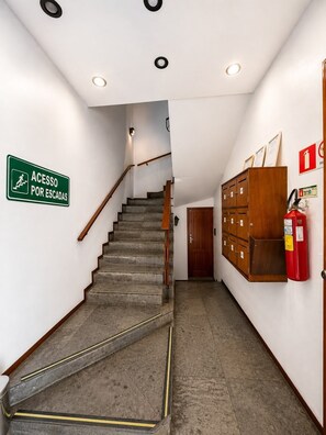 Un escalier menant à une pièce où se trouve un meuble en bois et un extincteur fixé au mur.