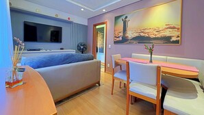 Una habitación de hotel moderna con cama, televisor, zona de comedor con mesa y sillas, y un cuadro grande en la pared.