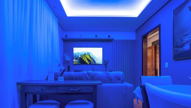 Una habitación moderna con un televisor de pantalla plana en la pared, un sofá, un escritorio con dos taburetes y una puerta que da a otra habitación.