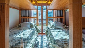 Una habitación con dos camas, vigas de madera, un ventanal grande y una alfombra estampada.