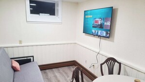A living room with a TV mounted on the wall, a window, a sofa, a dining table, and chairs. - 4 min walk to the beach. 1BD. Pets Ok FREE parking (Old Orchard Beach)