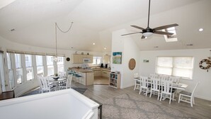 A spacious living area with a dining table, chairs, a kitchen in the background, and a ceiling fan. - Semi-Oceanfront, Private Pool, Hot Tub, Close to beach! WL1066, Schemering Seas (Corolla)