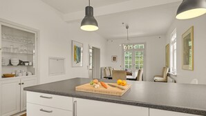 A modern kitchen with white cabinetry, a granite countertop, and a central island with fresh produce. There are pendant lights above the island and a dining area visible in the background. - Stunning home in Kværndrup with WiFi (Kværndrup)