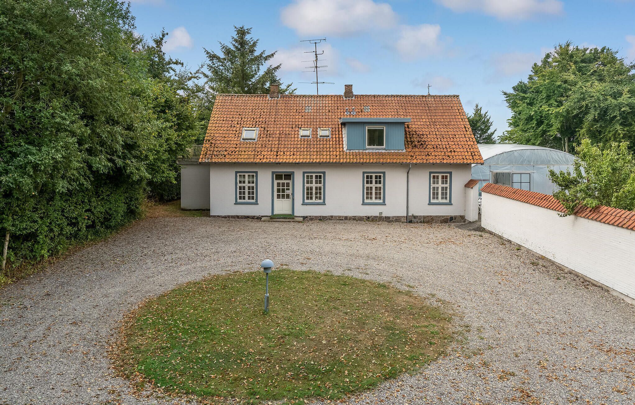 Une maison à deux étages, avec un toit en tuiles, un petit jardin et une allée gravillonnée.