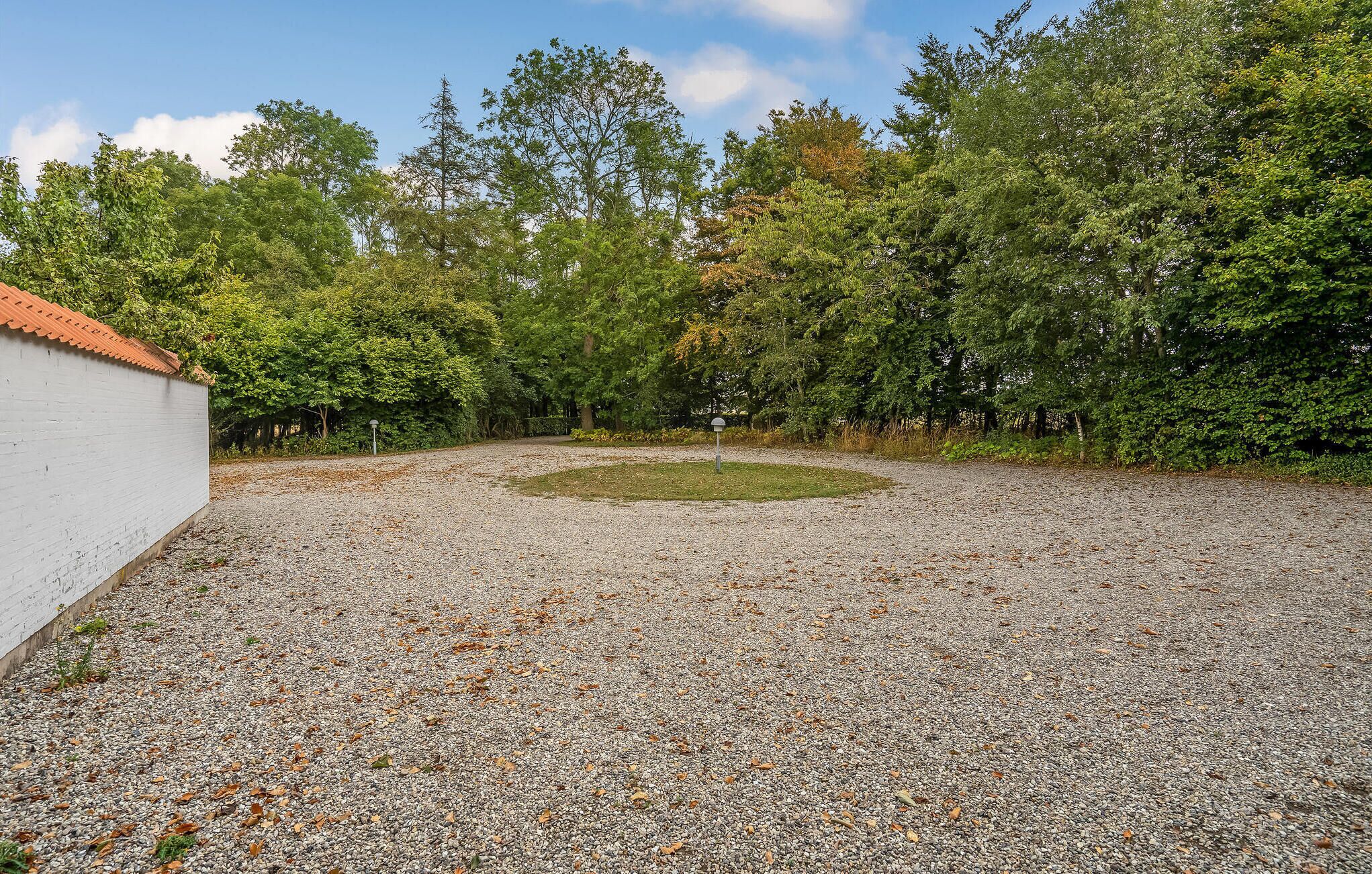 Een kiezelhofje met een witte muur aan de ene kant en dichte bomen op de achtergrond.