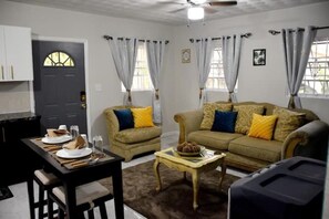 A living room with a sofa, armchair, coffee table, and a dining table set with plates and glasses.