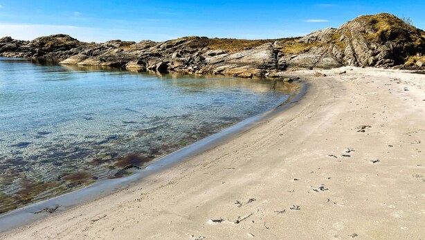 Une plage à l’eau claire, avec un rivage sablonneux et des affleurements rocheux.