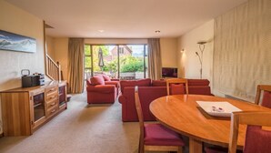 Una sala de estar con una mesa de comedor de madera, sofás rojos y un ventanal con cortinas.