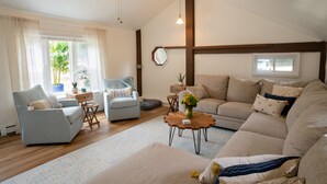 A spacious living room with a large sofa, a smaller armchair, a coffee table, and a ceiling fan. There are windows with curtains, a plant, and a view of the outdoors. - Dog friendly hideaway in Bucks County near River (Bensalem)