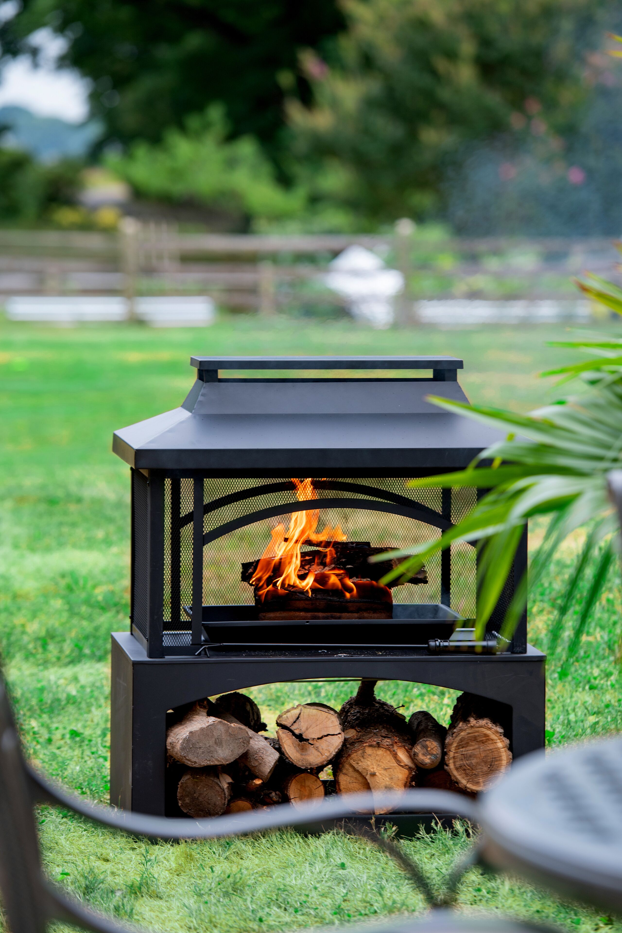 Un hoyo de fuego exterior negro con fuego encendido, rodeado de leña y hierba.