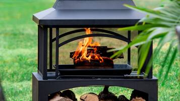 Un hoyo de fuego exterior negro con fuego encendido, rodeado de leña y hierba.