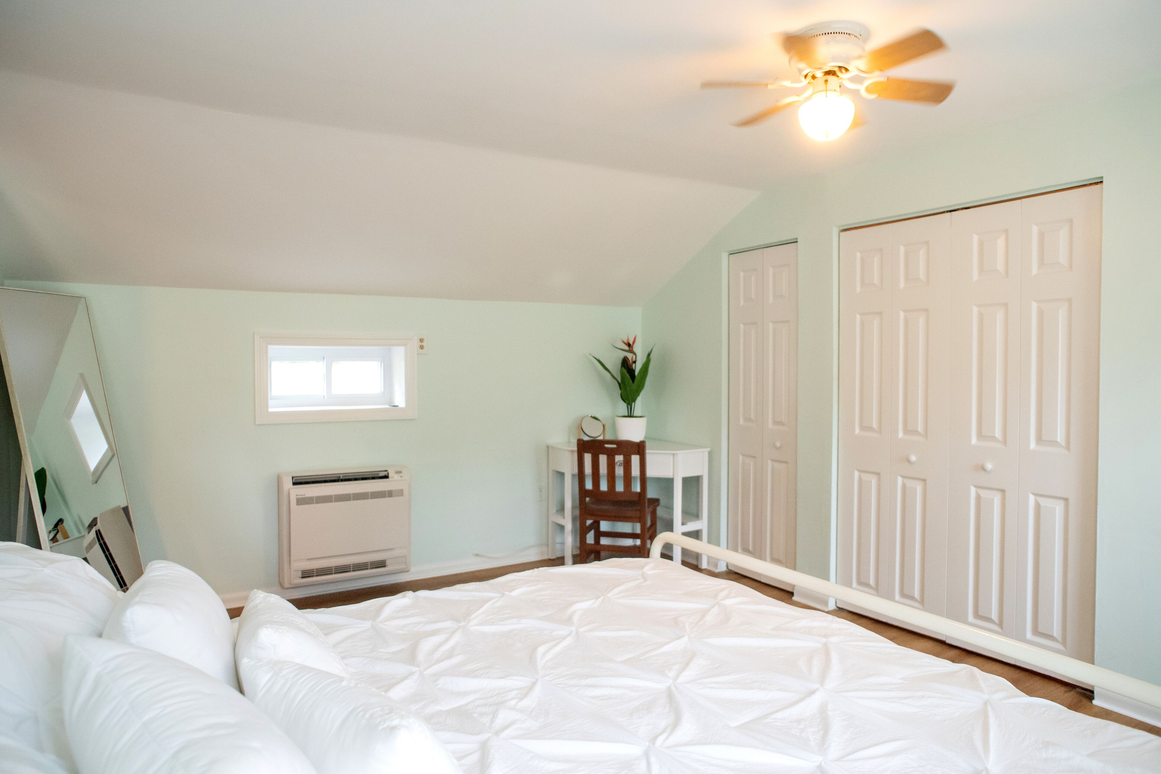 A bedroom with a bed, a desk, a chair, a ceiling fan, and a closet.