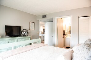 A bedroom with a bed, a dresser, a television, and a fan.