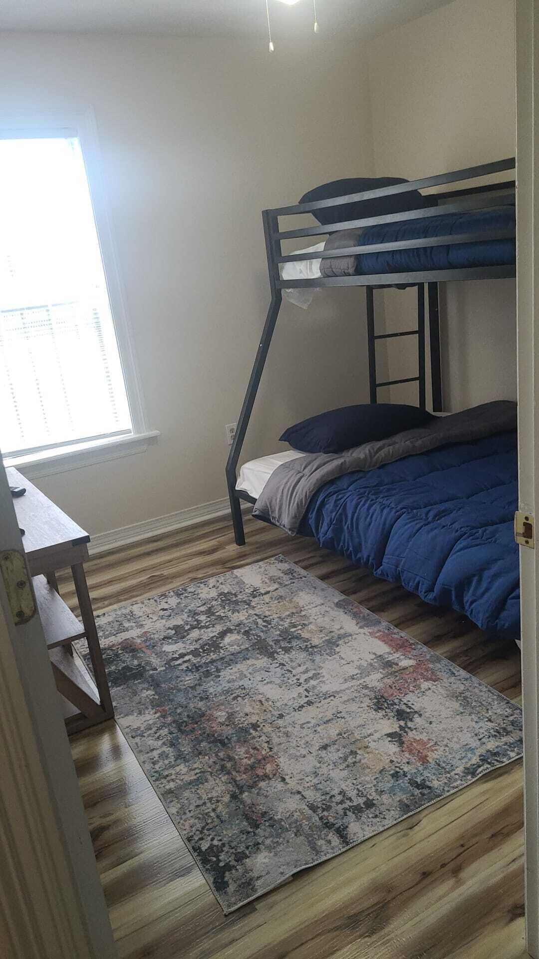 Une chambre avec un lit superposé, un petit bureau et une fenêtre.