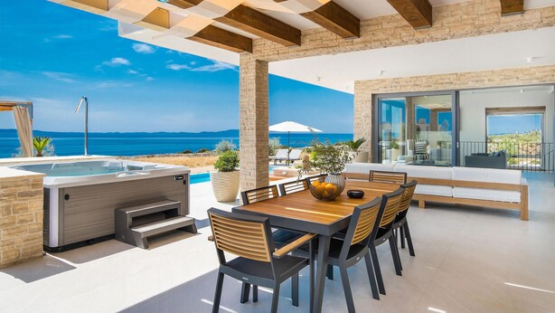 Un espacio moderno al aire libre con zona de comedor, piscina, jacuzzi y vistas al mar.