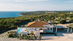 Una villa moderna con piscina, un porche cubierto y vistas al mar y al paisaje circundante.