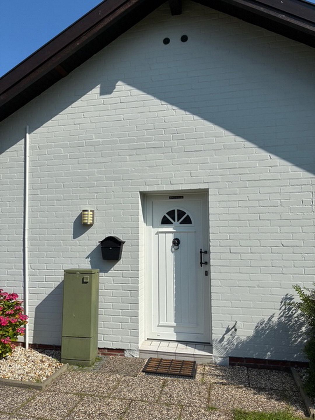 Ein weißes Backsteinhaus mit einer weißen Tür, einem kleinen Fenster und einer grünen Verteilerbox.