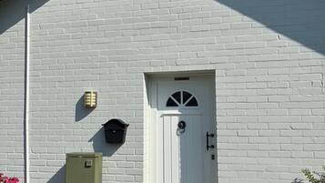 Ein weißes Backsteinhaus mit einer weißen Tür, einem kleinen Fenster und einer grünen Verteilerbox.