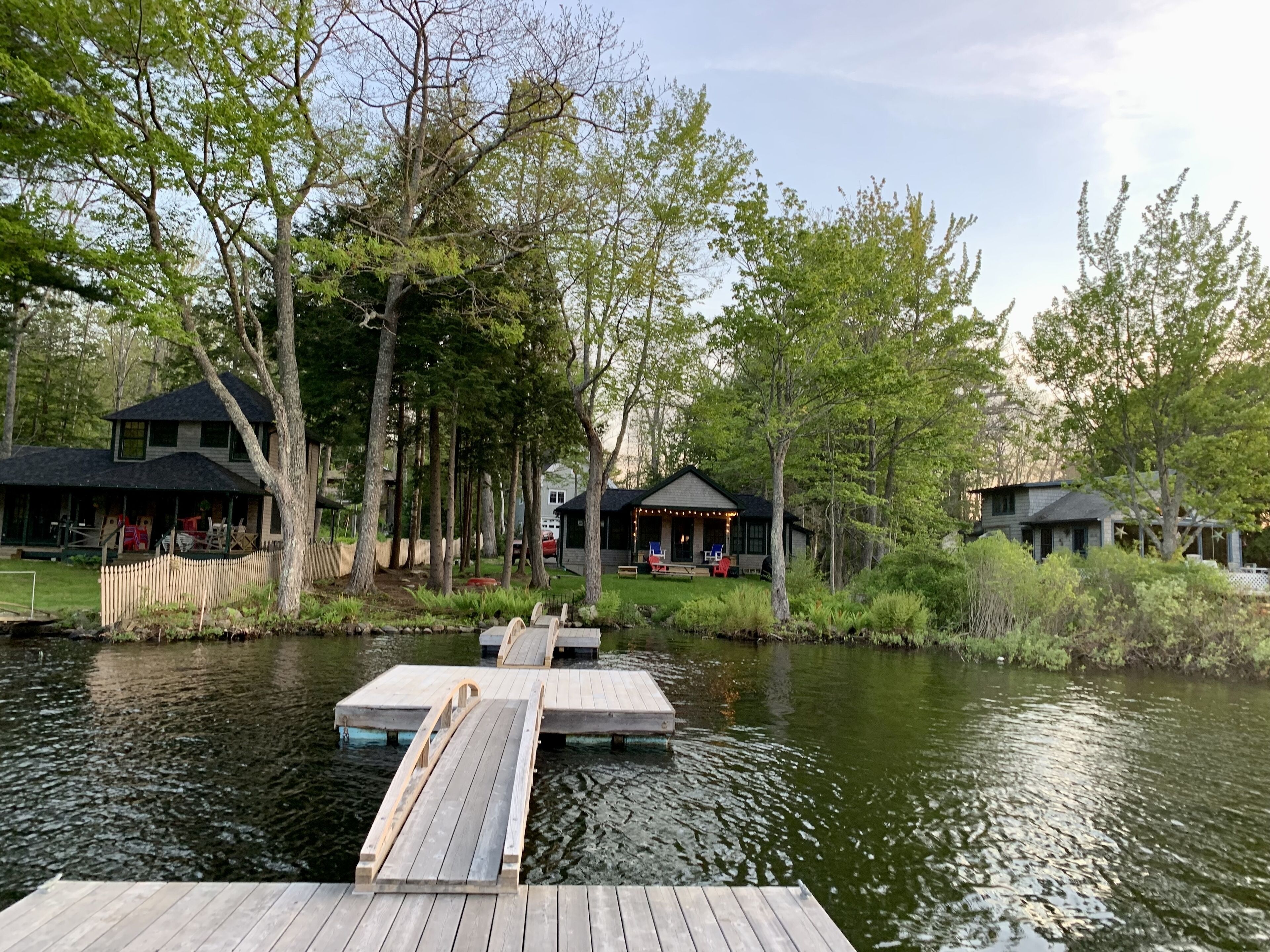 Une jetée en bois s’étendant sur un lac paisible, entourée d’arbres et de deux petites cabanes dotées d’un espace extérieur aménagé pour s’asseoir.