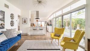 A modern living room with a blue sofa, yellow chairs, and a kitchen in the background. - Original Donald Wexler Midcentury Gem with Pool in famous East Moviestar Colony (Palm Springs)
