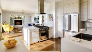 A modern kitchen with a central island, stainless steel appliances, and a dining area with a yellow chair. - Original Donald Wexler Midcentury Gem with Pool in famous East Moviestar Colony (Palm Springs)