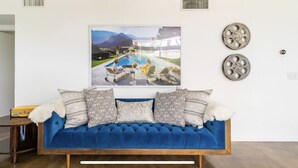 A blue sofa with patterned cushions, a framed landscape painting above it, and decorative metal pieces on the wall. - Original Donald Wexler Midcentury Gem with Pool in famous East Moviestar Colony (Palm Springs)