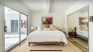 A bedroom with a large bed, a sliding glass door leading to an outdoor area, and a large mirror reflecting the room. - Original Donald Wexler Midcentury Gem with Pool in famous East Moviestar Colony (Palm Springs)