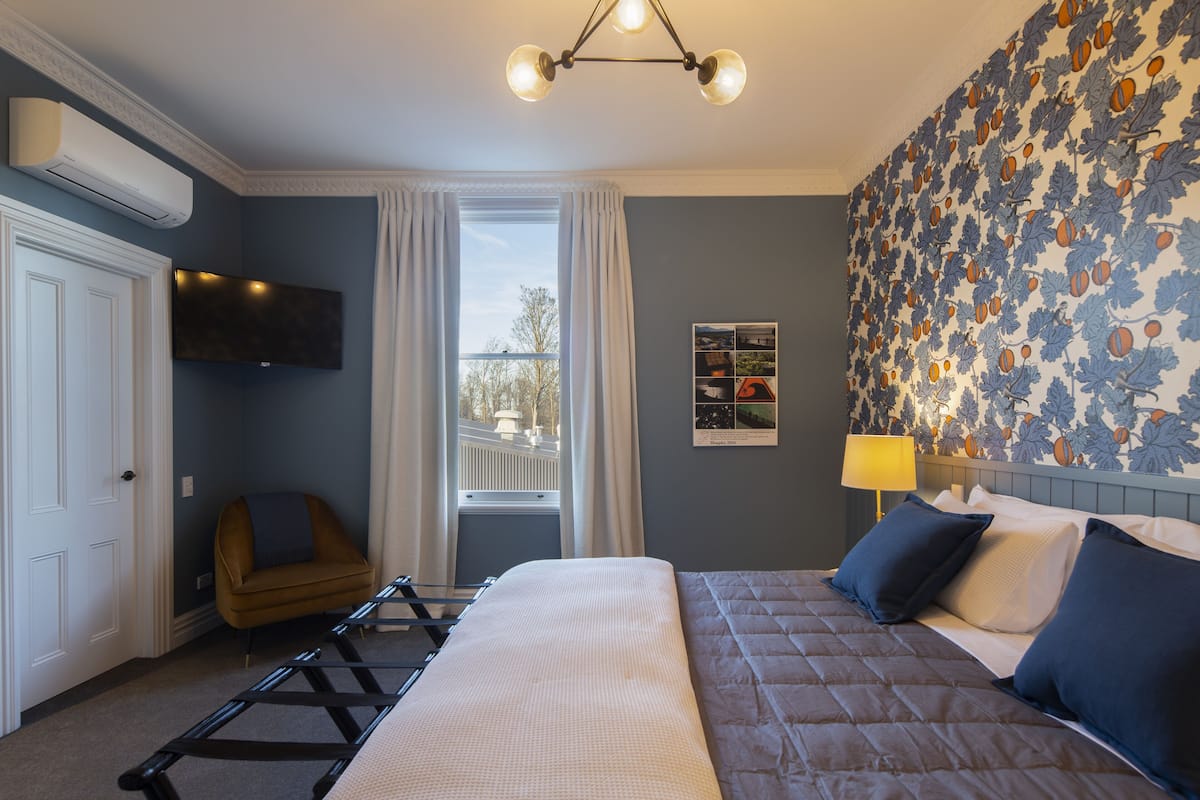 A bedroom with a bed, a chair, a TV, a window, and a wall with a floral pattern.