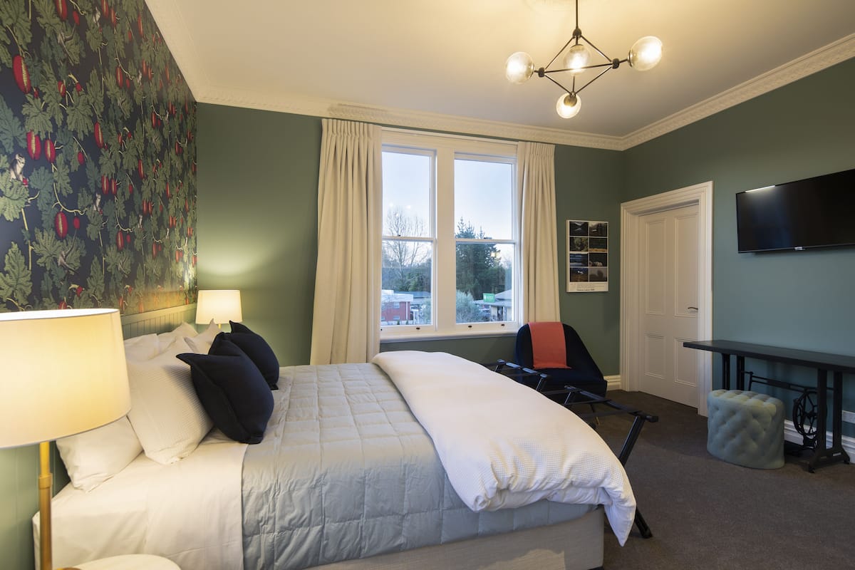 A bedroom with a bed, a desk, a chair, a television, and a window with curtains.