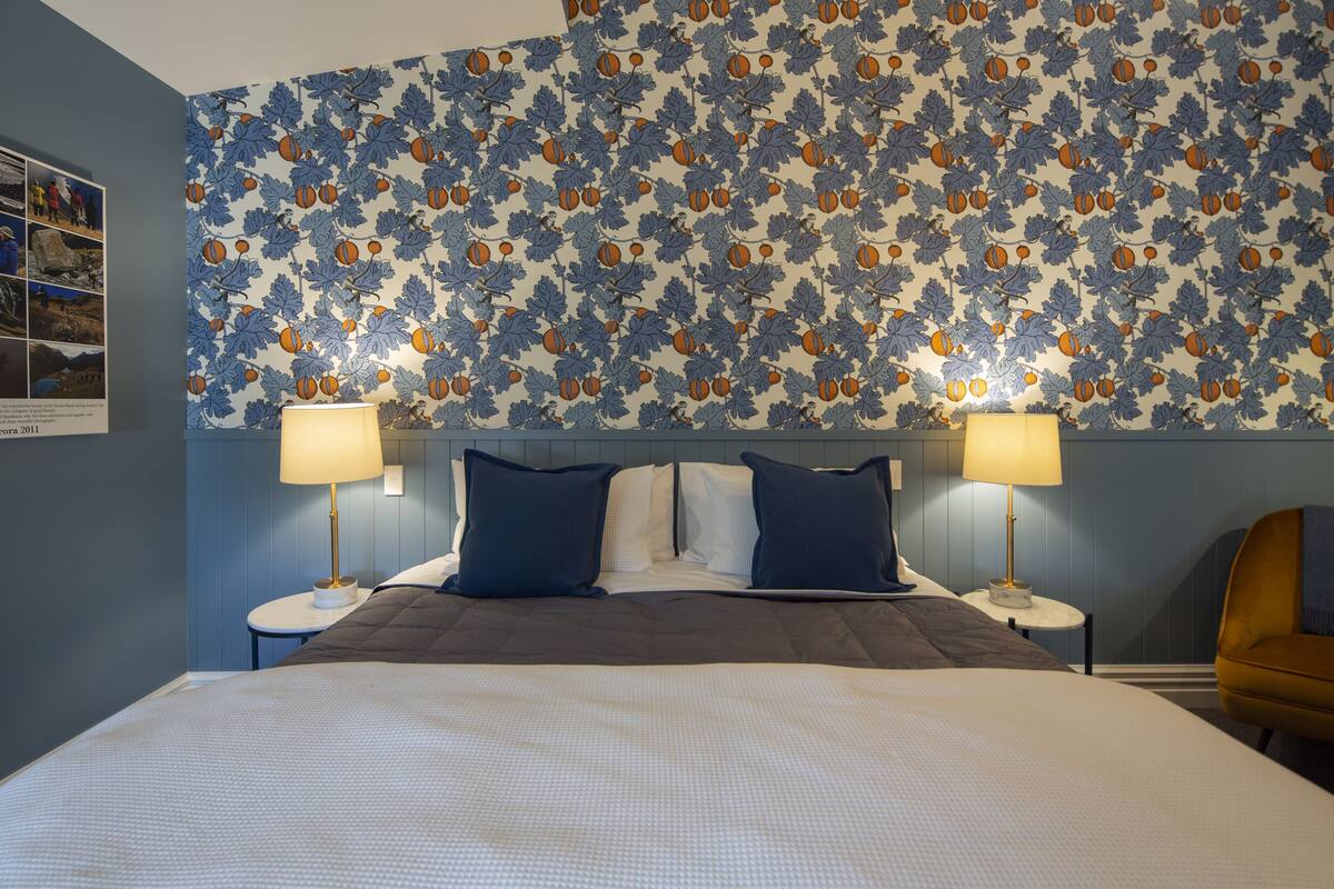 A hotel room with a large bed, two bedside tables with lamps, a headboard with a leaf pattern, and a small armchair.