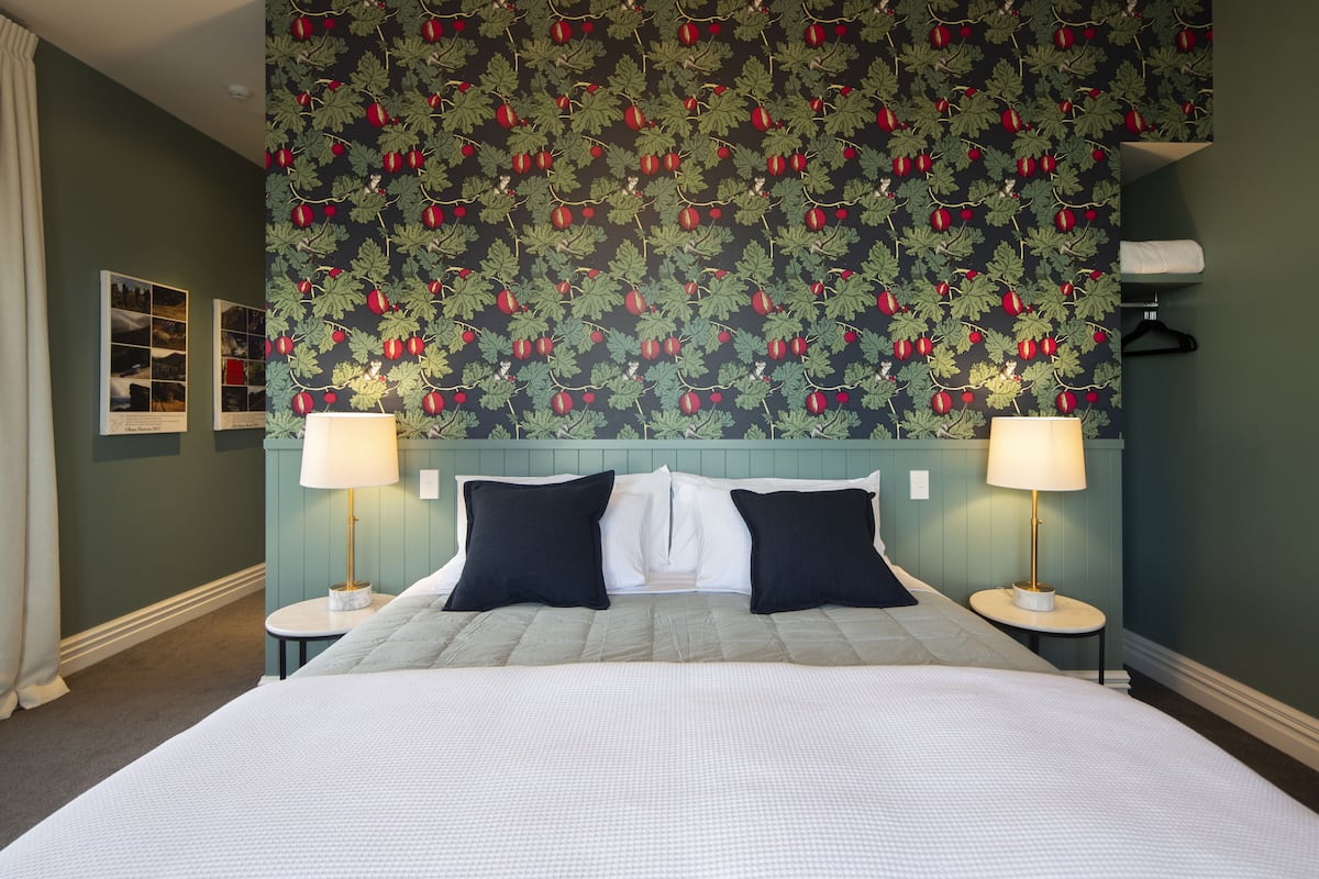 A hotel room with a large bed, two bedside tables, and a wall with a leaf and fruit pattern.