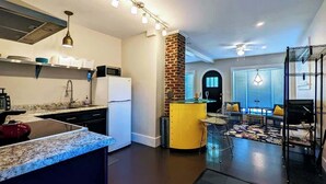Una cocina moderna con una isla central, un comedor con una pared de acento amarilla y una sala de estar con un mueble de televisión negro.