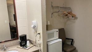 A hotel room with a sink, a coffee maker, a microwave, a hair dryer, and a chair.