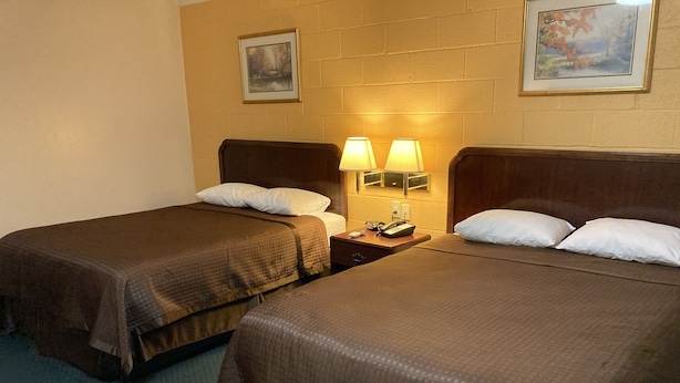 A hotel room with two beds, each with a pillow and a blanket. There is a nightstand with a lamp and a phone.