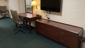 A hotel room with a wooden desk, a chair, a television mounted on the wall, and a mirror.