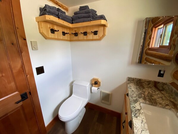 Un baño con inodoro blanco, un perchero de madera y una ventana con vistas.