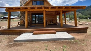 Eine rustikale Holzhütte mit Kamin aus Stein, einer Veranda und einer Betonplattform davor.