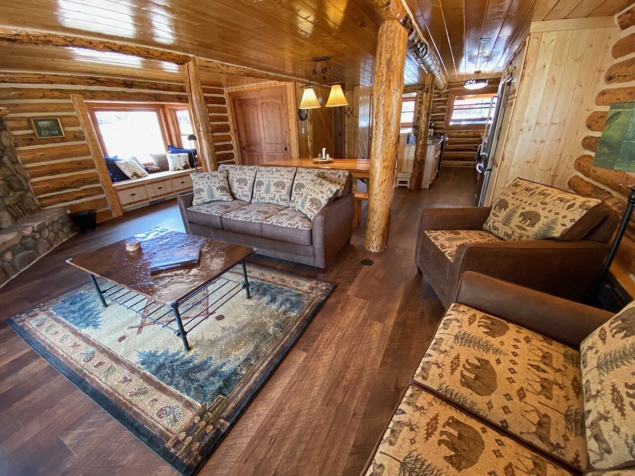 Een blokhutinterieur met een bank, fauteuils, een salontafel en een vloerkleed.