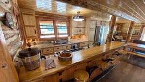 Ein Holzblockhaus im Inneren mit einer Küchenzeile, die einen großen Herd, ein Spülbecken und eine Theke mit Hockern umfasst.