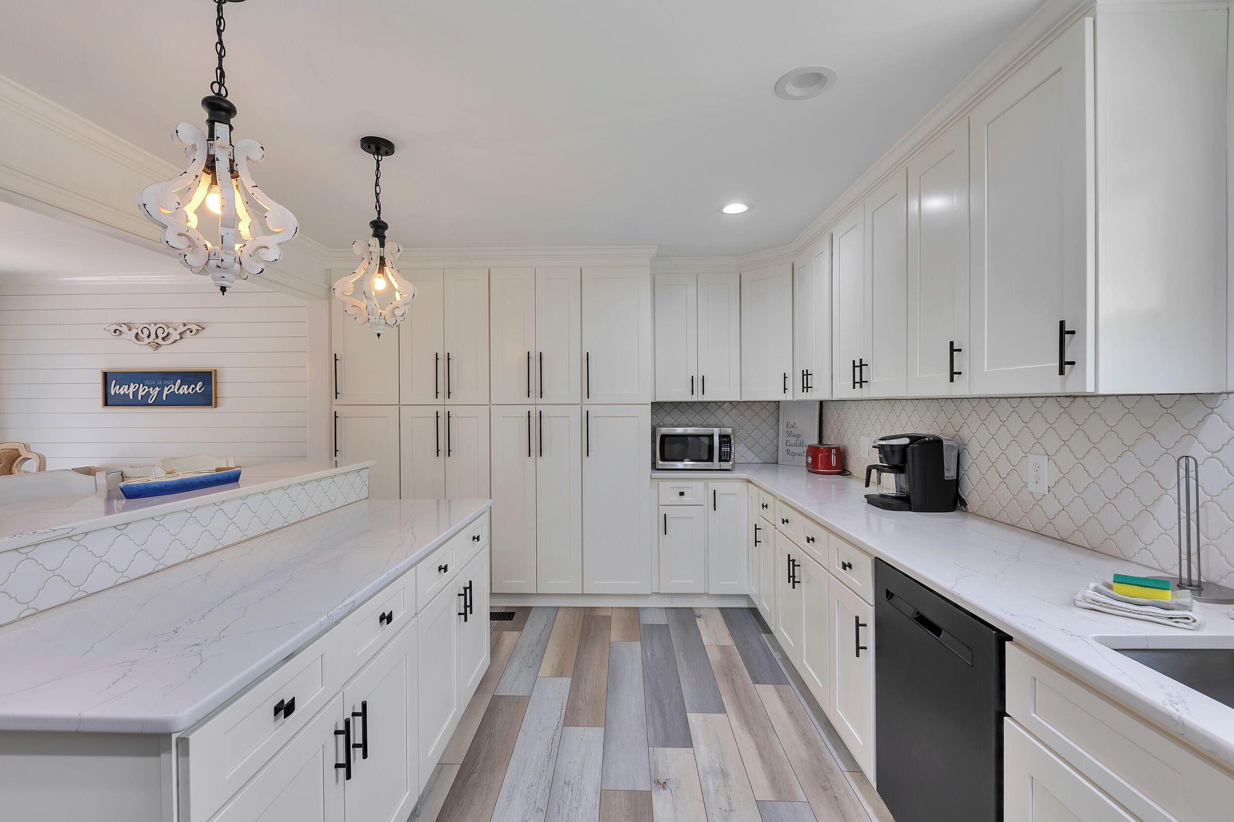 A modern kitchen with white cabinetry, a marble countertop, a microwave, a coffee maker, and a dishwasher.