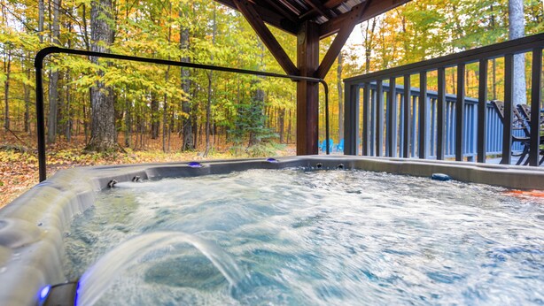 A hot tub with a wooden deck and railing, surrounded by trees in autumn colors. - Total Seclusion! Hot tub,  Traverse City downtown 10 min, Booking for summer!  (Traverse City)